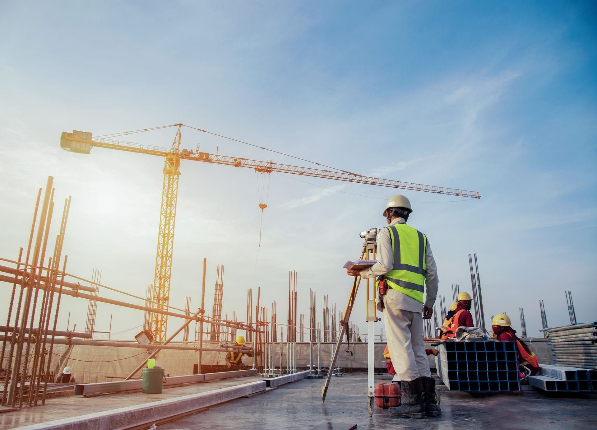 Vermessungsingenieur mit Theodolith auf einer Baustelle mit Kran und Arbeitern